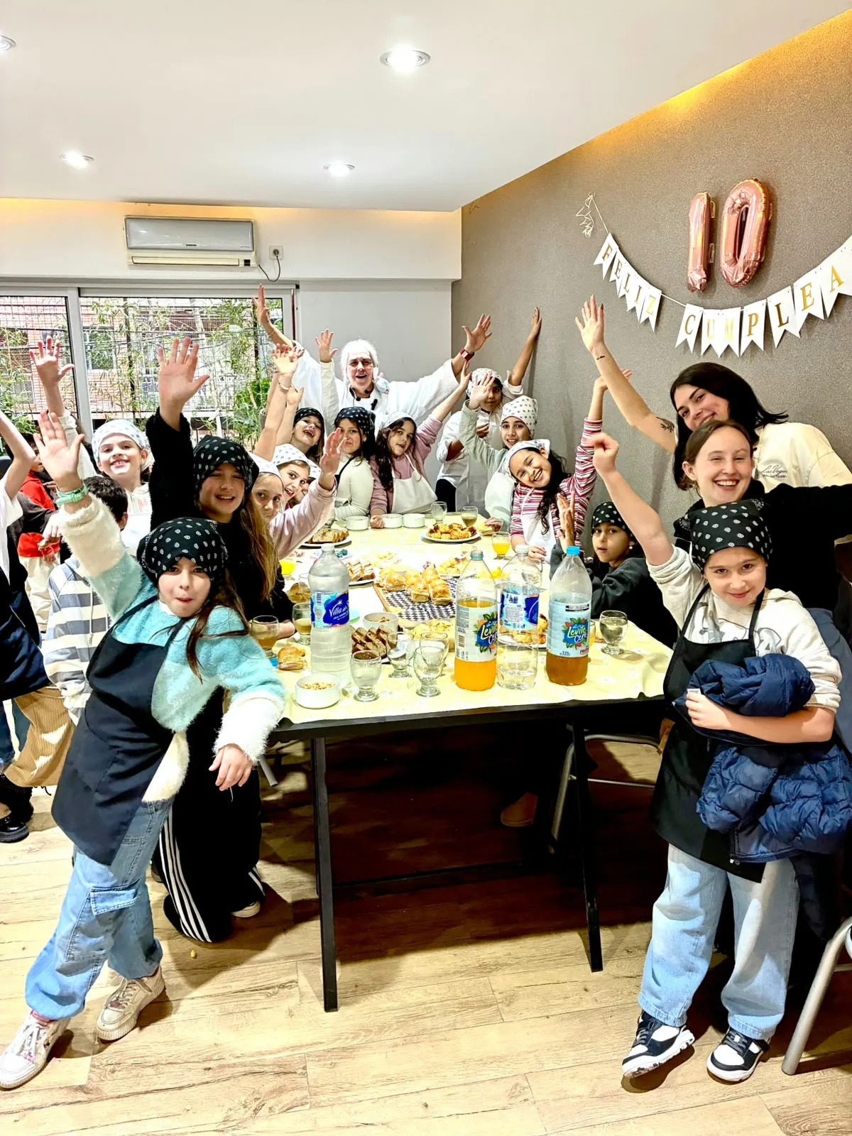 Un grupo grande de chicos con los brazos en alto alrededor de la mesa